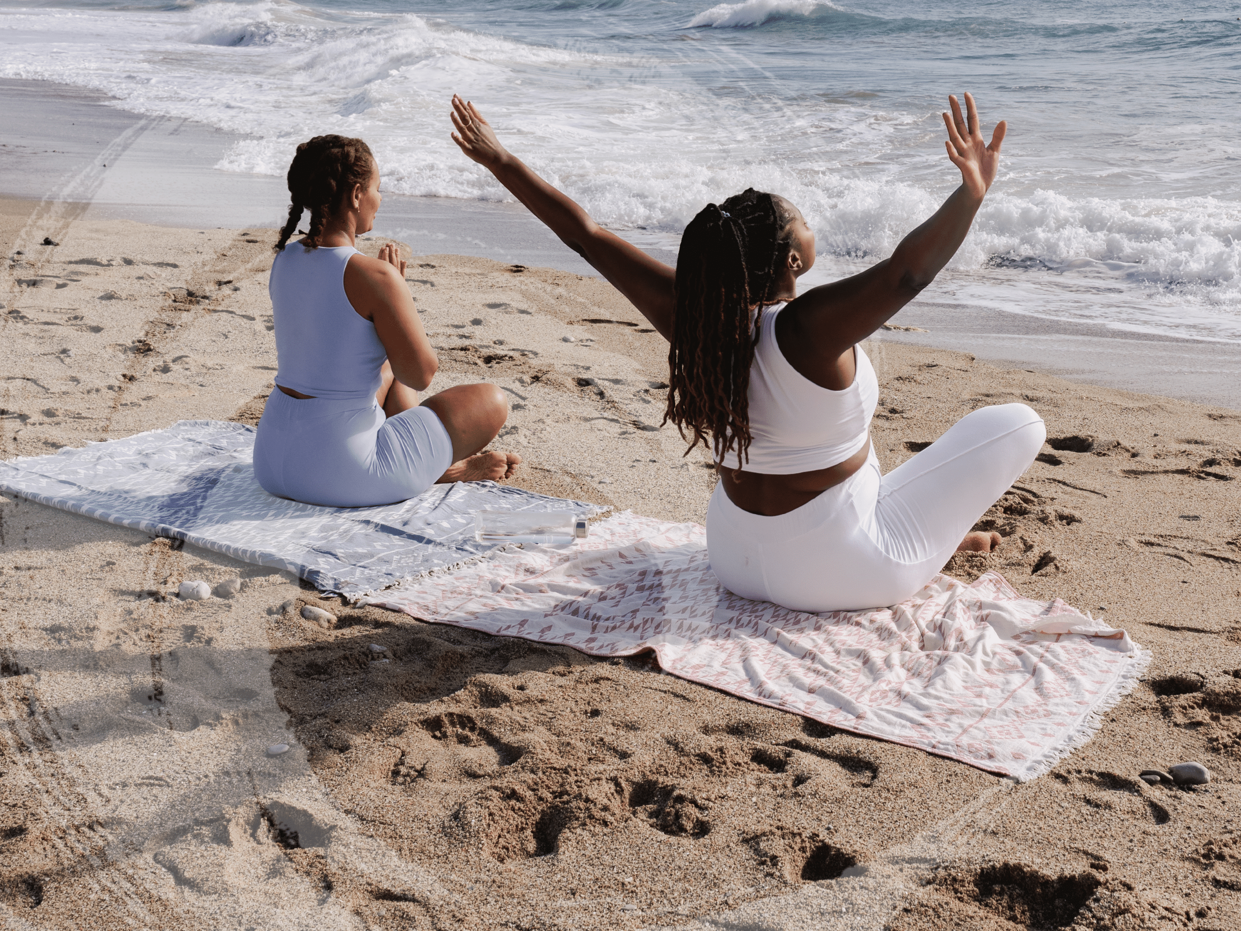 Two women sitting at the beach with arms outstretched, representing BIPOC mental health