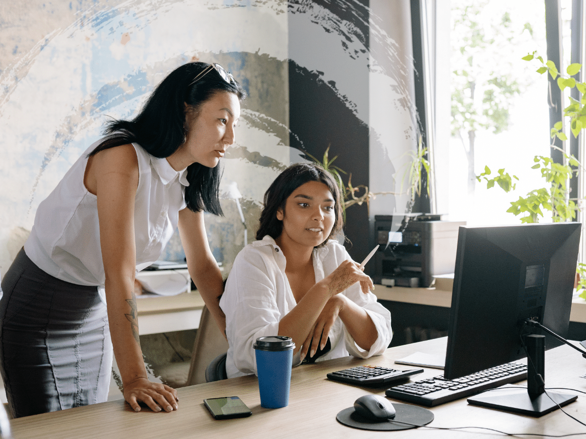 Two women looking at the same computer monitor, symbolizing being overstimulated at work