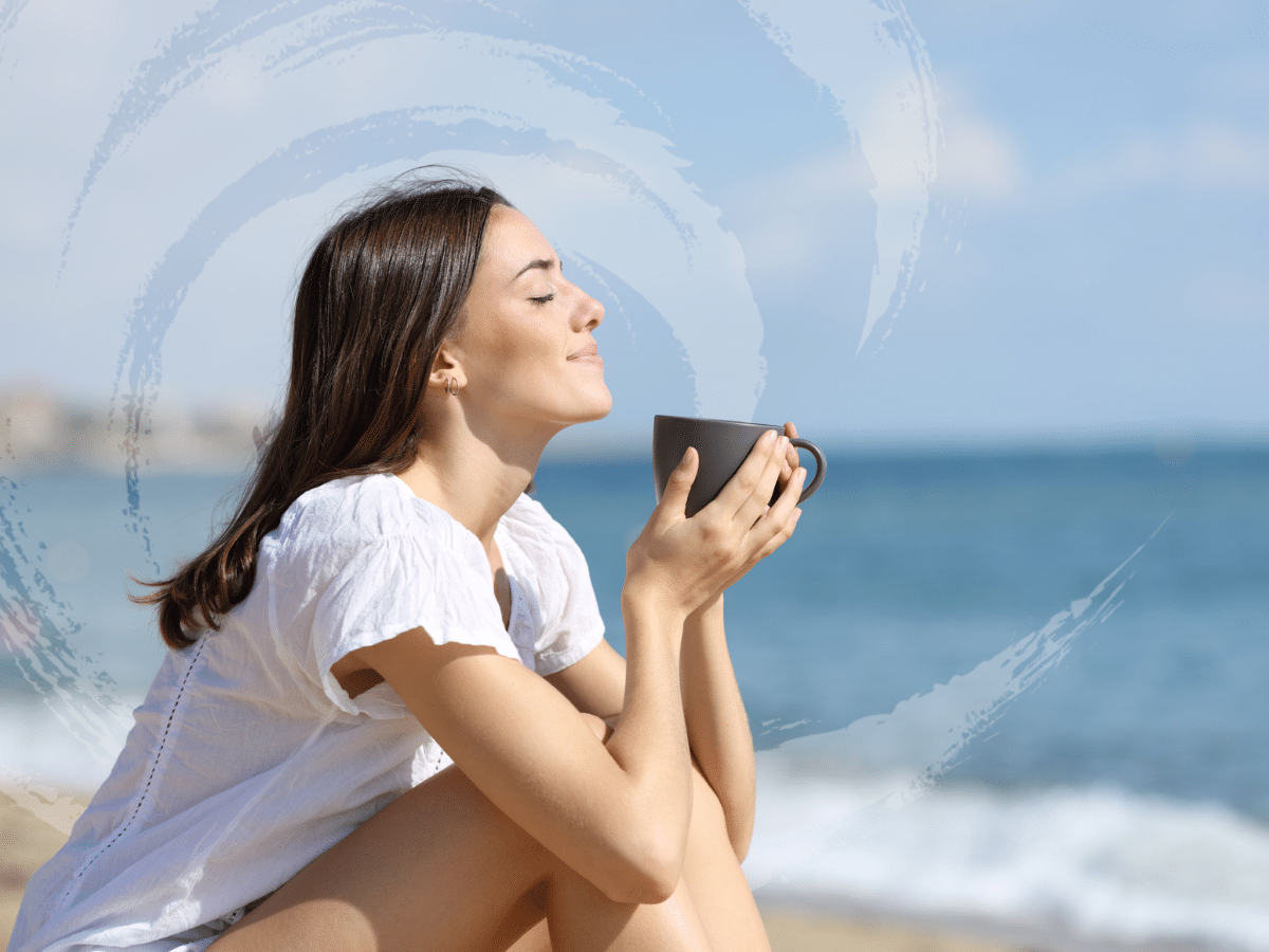 A woman sits at the beach cupping a beverage in her hand, symbolizing a common question what does a psychiatrist do